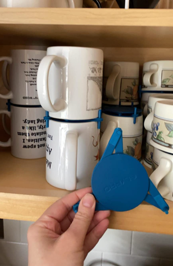 reviewer holding stacker contraption in front of organized mug cupboard