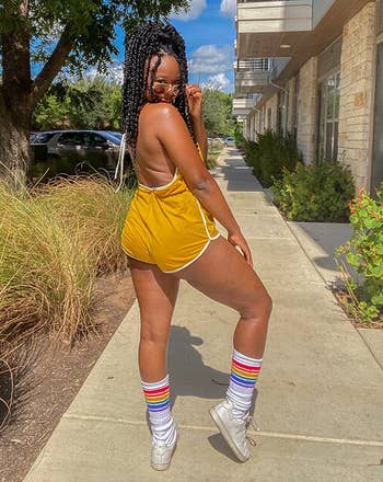 Person outdoors successful sporty outfit and sunglasses, wearing sneakers and rainbow-striped socks, posing confidently connected a sidewalk