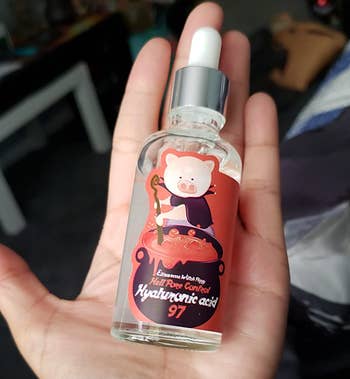 reviewer holding a bottle of the serum with a pig witch illustration on it 