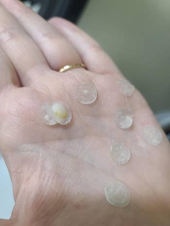 A hand showing seven peeled-off skincare product patches, one with a white residue, indicating their performance