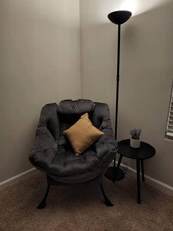 Reviewer image of dark gray tufted plush chair with yellow throw pillow next to a side table and floor lamp