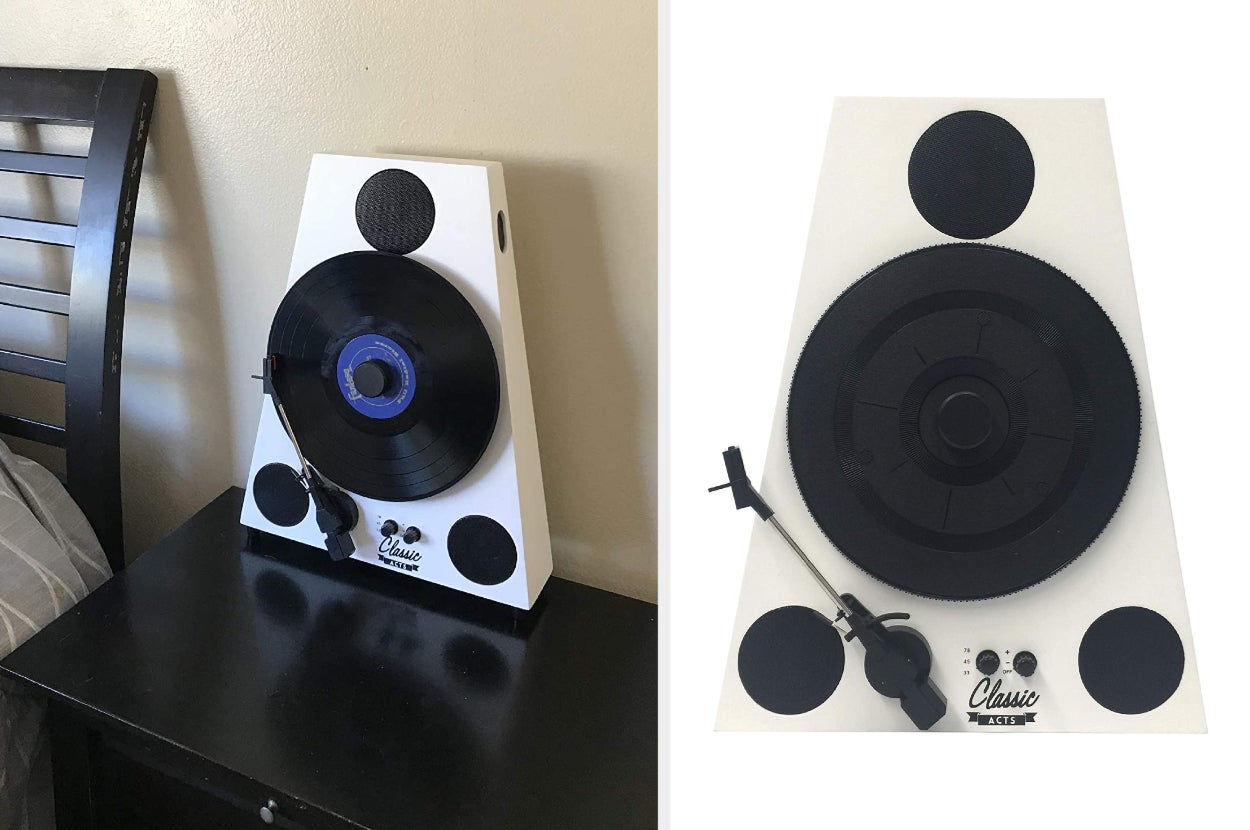 White and black vertical turntable with three black built-in circular speakers and two adjustable knobs on top of black side table, close up of product on a white background