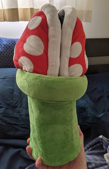 a reviewer holding the slippers stored in the included green plush pipe 