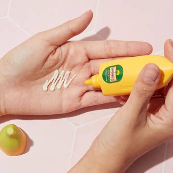 Hands applying cream from a banana-themed lotion bottle onto a palm, with a small banana-shaped cap nearby