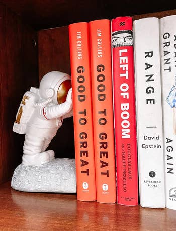reviewers astronaut figurine holding up books on a shelf
