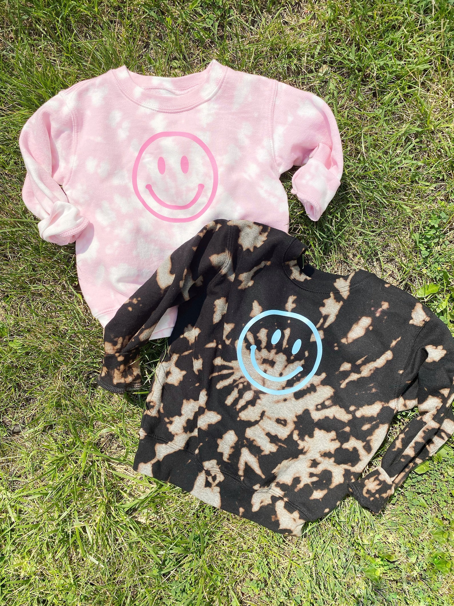 a pink acid wash sweatshirt and a brown acid wash sweatshirt both with smiley faces on it