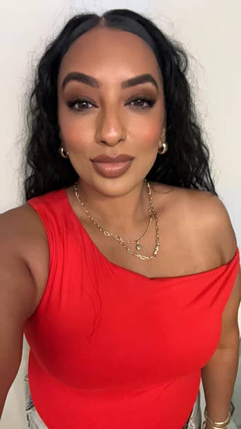 Person successful  a one-shoulder top, layered necklaces, and hoop earrings poses for a buying  article