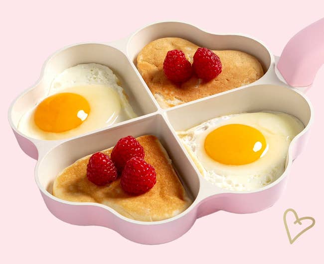 Pink heart-shaped silicone mold with sections for making pancakes and eggs, shown with pancakes, eggs, and raspberries inside