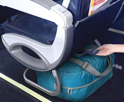 model placing passport on top of blue duffel, which is under the airplane seat in front of them