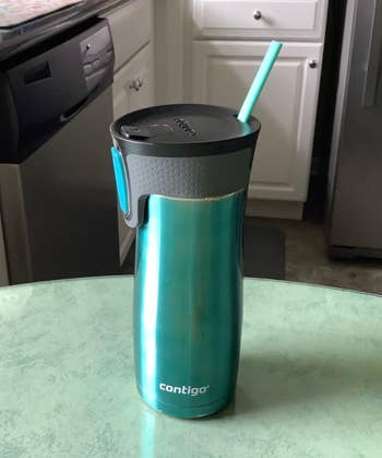 travel mug with an oval shaped green straw poking out of it 
