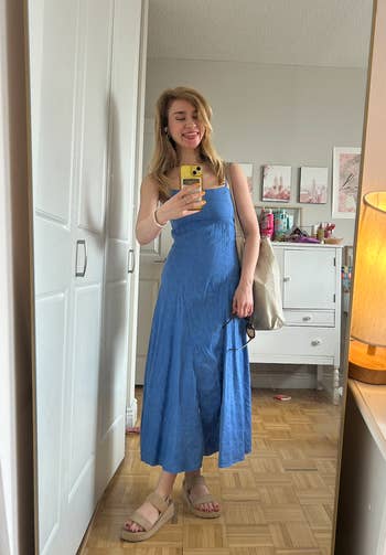 A writer   successful  a bluish  sundress and sandals takes a reflector  selfie, smiling