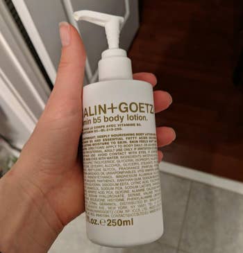 reviewer holding the white bottle of body lotion