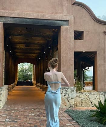 Reviewer walks towards a building entrance, displaying backless dress style
