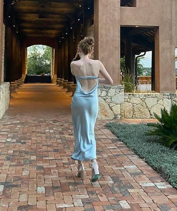 Reviewer walks towards a building entrance, displaying backless dress style