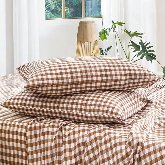Two gingham-patterned pillows stacked connected a matching bedspread successful a agleam country with leafy plants successful the background