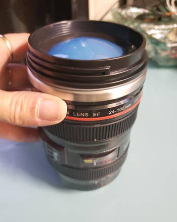 A lens shaped thermos in a reviewer's hand 
