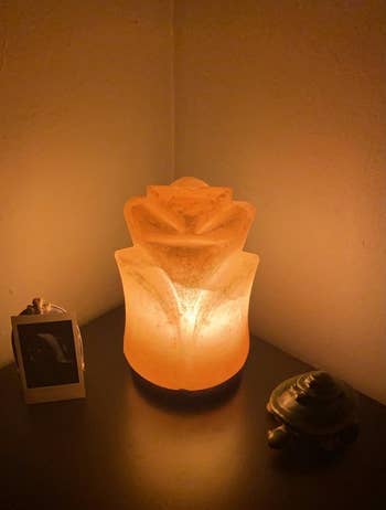 another reviewer's rose-shaped salt lamp brightly lit in a dark room