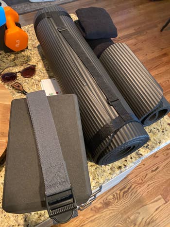 Yoga mats, a yoga artifact  with strap, dumbbells, sunglasses, and a tiny  foam mat connected  a room  countertop