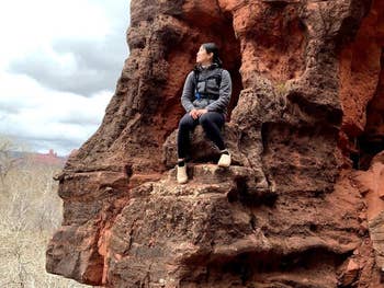 Person sitting connected  a rocky ledge, wearing casual outdoor covering  and sneakers, gazing into the region  amidst a earthy  landscape