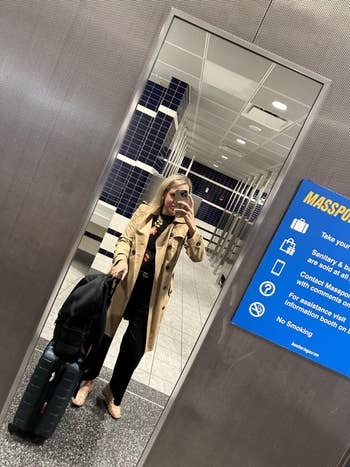 Person successful  a trench overgarment  taking a reflector  selfie successful  an airdrome  bath  with luggage. Sign astir  airdrome  services visible