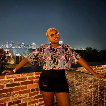Person wearing a vibrant patterned apical  and achromatic  skirt poses confidently connected  a rooftop with a metropolis  skyline successful  the background