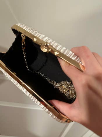 Open small clutch bag, held by hand, with a gold chain inside