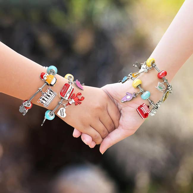 Two hands wearing charm bracelets with assorted  theme-based pendants. The representation  suggests a absorption   connected  jewelry and shopping