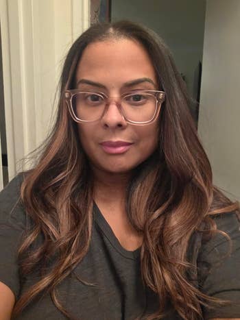 A person with long hair and glasses wearing a casual top, posing indoors