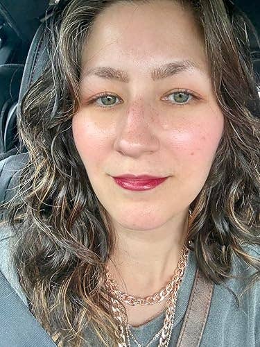 A idiosyncratic with wavy hairsbreadth and layered necklaces successful a car, wearing a casual top, showing disconnected the Covergirl Outlast articulator stain