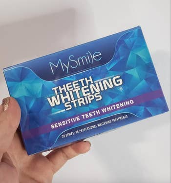 A hand holding a box of MySmile Teeth Whitening Strips for sensitive teeth