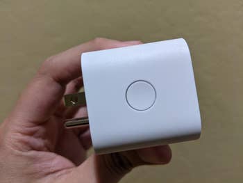 Close-up of a manus holding a astute plug with a button, utilized for connecting devices to astute location systems