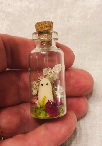 A small ghost in a tiny jar with flowers around it 