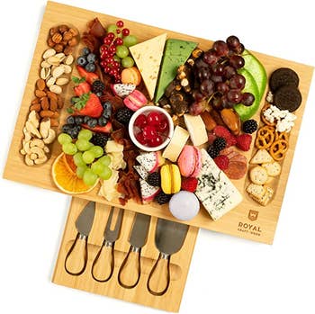 A charcuterie board with cheese, crackers, fruit, and nuts and the knife drawer pulled out underneath