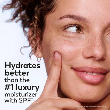 Close-up of a smiling idiosyncratic applying moisturizer to their cheek, with substance claiming superior hydration compared to apical luxury SPF moisturizers