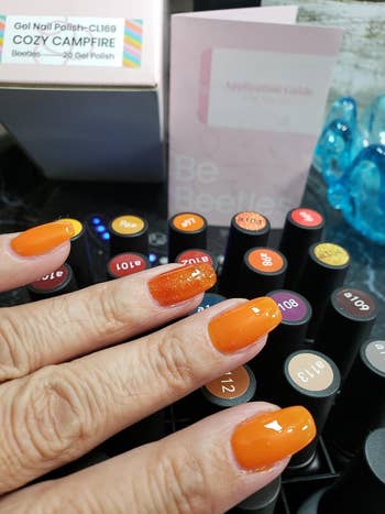 reviewer's nails painted orange with kit and polish bottles in the background