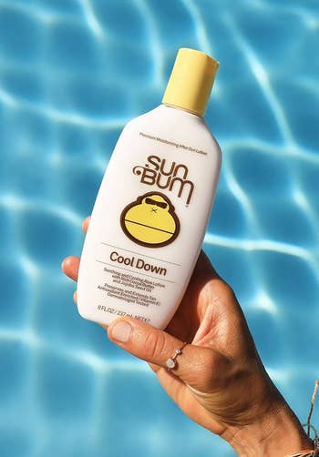 Tangan Memegang Bum Sun Cool Down Lotion di dekat kolam