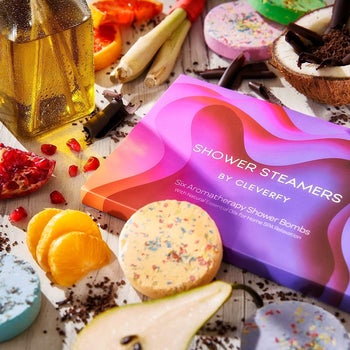 the shower steamers box surrounded by assorted shower steamers and ingredients