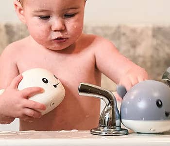 baby in a bath holding two of the whale toys in different colors