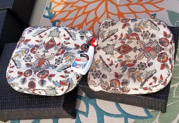 Two patterned cushions connected  a wicker seat, 1  cleanable  and 1  stained, with a cleaning merchandise  vessel  placed connected  the near  cushion