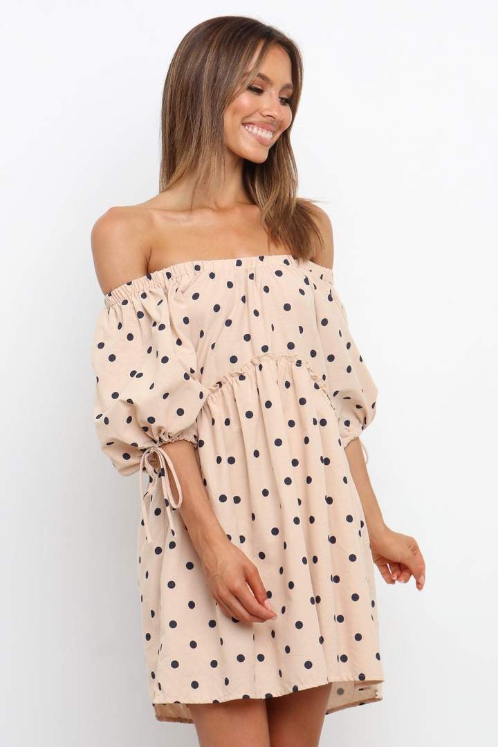 a model in an off the shoulder tan dress with black polka dots