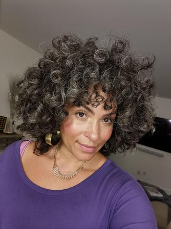 a reviewer with voluminous curly hair and hoop earrings, wearing a necklace and a purple top