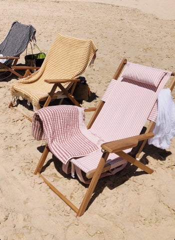 three tommy chairs lined up on a beach with towels draped over them