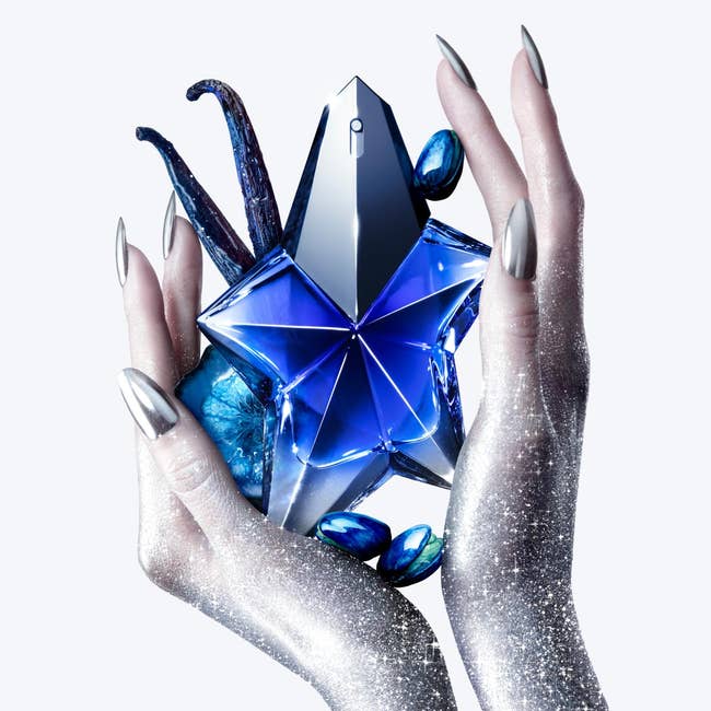 Hands with metallic nails clasp a star-shaped perfume bottle, surrounded by decorative elements, evoking a luxurious and modern buying experience