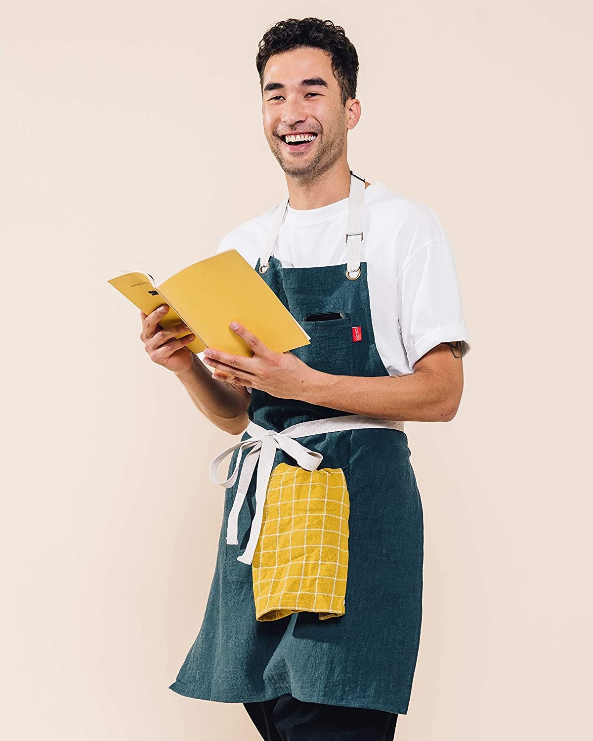 model smiling while wearing apron and holding dish towel and recipe book