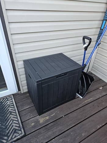 Outdoor storage box on a deck with cleaning tools nearby.