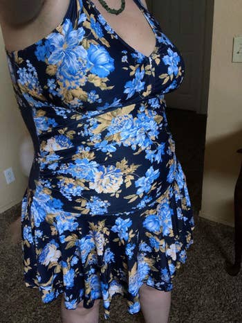 Person wearing a floral blue swim dress with a ruched waist and flared skirt. 