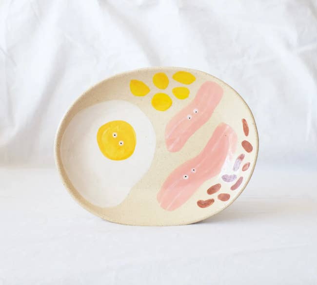 The serving plate with an egg and two slices of bacon painted on, all have tiny eyes