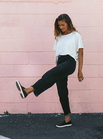 Model wearing the sneakers in black in front of a pink wall kicking their feet