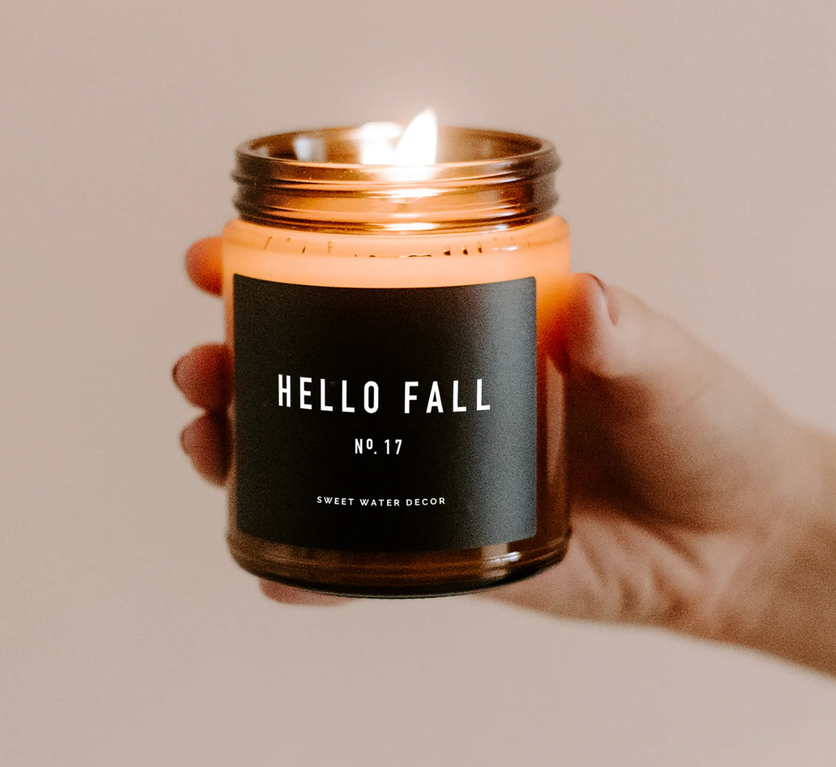 a model's hand holding a lit fall candle
