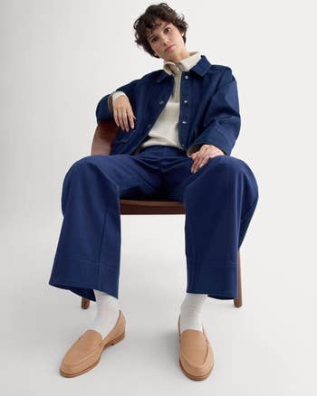 Person seated wearing a casual denim jacket, wide-leg pants, and loafers, showcasing a relaxed and effortless style